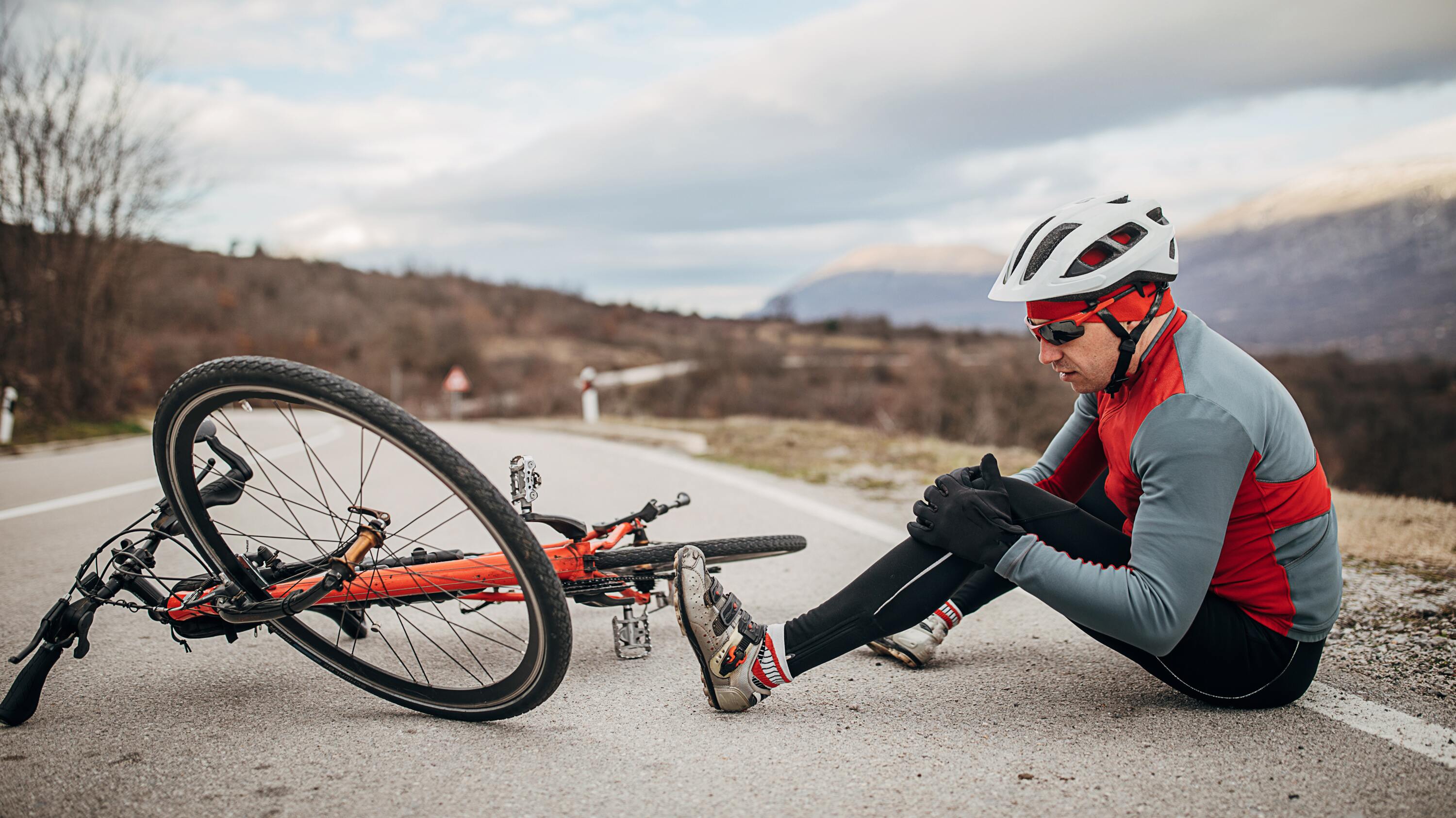 Male cyclist sitting next to crashed bike